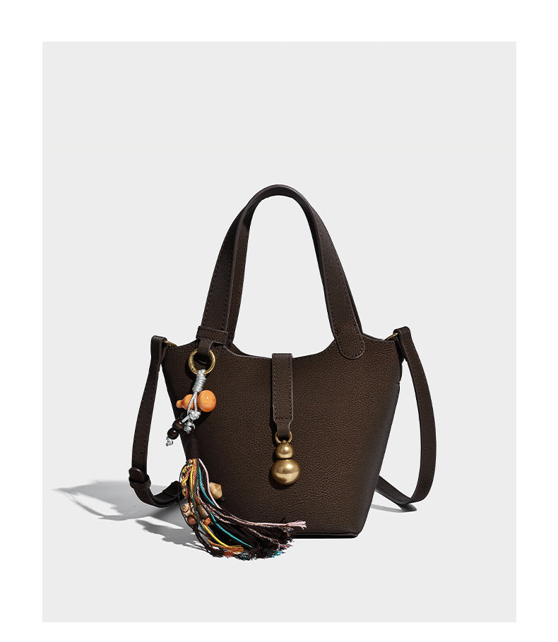 Kleine matte Beuteltasche mit genarbter Oberfläche, antikgoldfarbenen Ringbeschlägen, Perlen- und Quastenanhänger, kurzen Tragegriffen oben und
