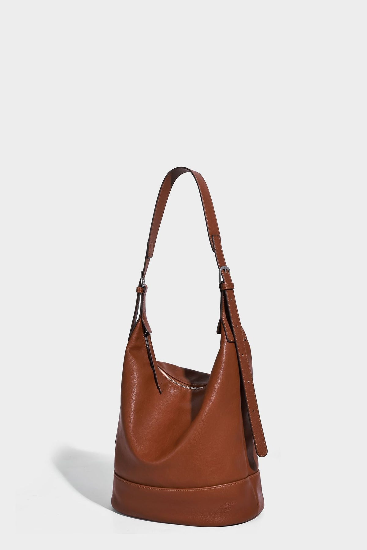Slouchy bucket hobo shoulder bag in dark brown with glossy leather-look finish, top zip closure, and long adjustable, detail