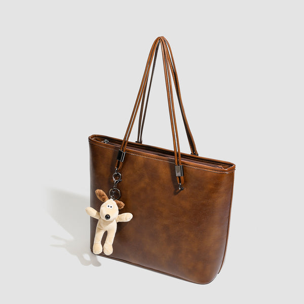 Large structured brown vintage-finish tote bag with double shoulder handles, gunmetal hardware, and plush bear charm, detail