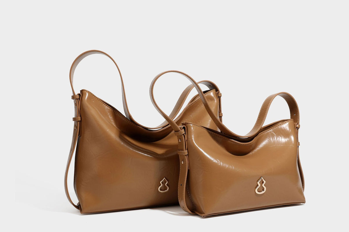 Lässig fallende Hobo-Schultertasche mit offenem Oberteil aus glänzender, karamellbrauner Lederoptik, mit Logo-Beschlägen in Goldoptik und langem, verstellbarem