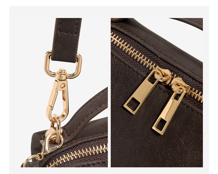 Compact boxy mini handbag with matte pebbled finish, dual top zipper, short top handle, side tassel charm, and gold-tone