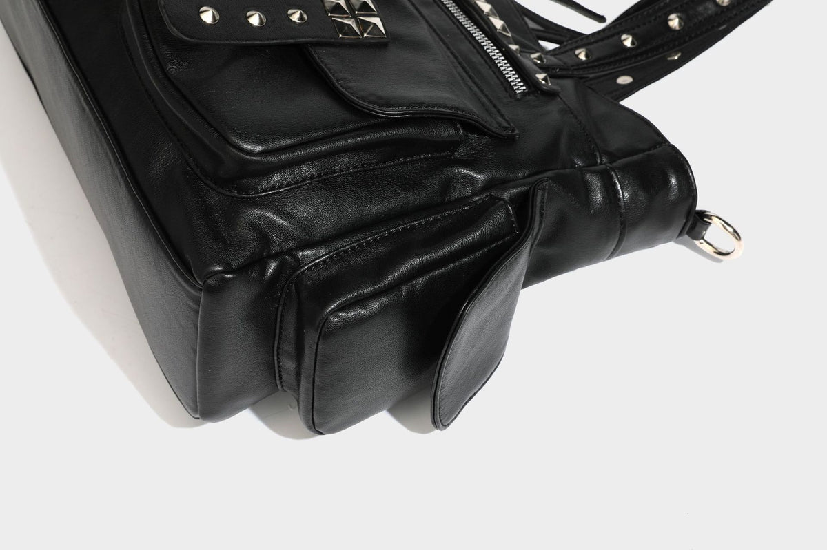 Black leather-look tote bag with silver pyramid studs on handles and front panel, multiple flap and zip exterior pockets