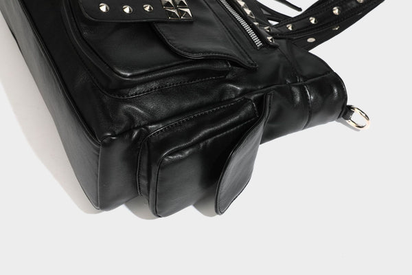 Black leather-look tote bag with silver pyramid studs on handles and front panel, multiple flap and zip exterior pockets