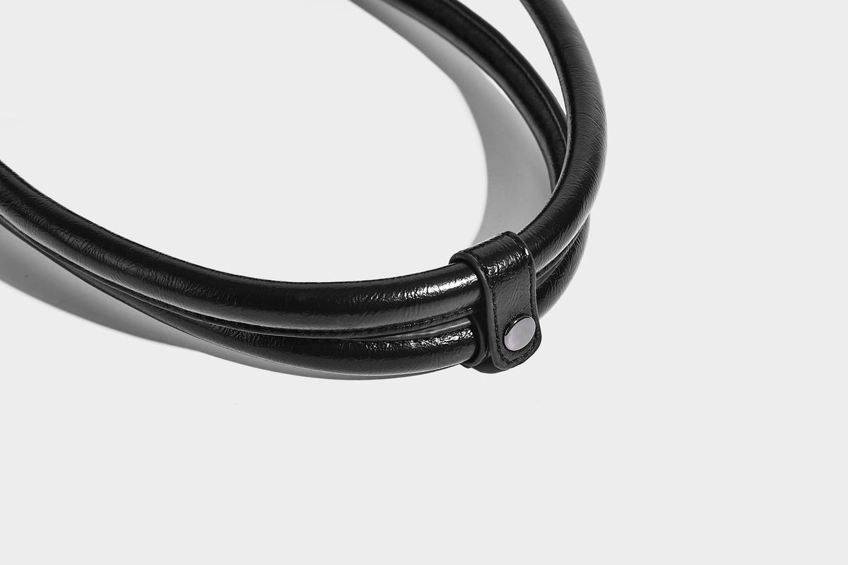 Längliche Schultertasche in Zylinderform mit glänzender Lederoptik, silberfarbenen Nietenbeschlägen, seitlichen Quasten und mehreren außenliegenden Reißverschlüssen