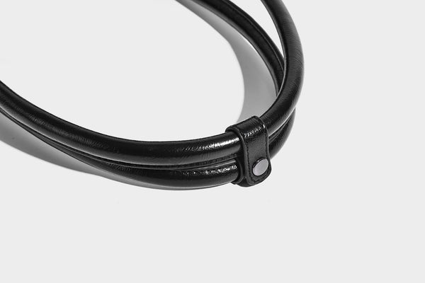 Längliche Schultertasche in Zylinderform mit glänzender Lederoptik, silberfarbenen Nietenbeschlägen, seitlichen Quasten und mehreren außenliegenden Reißverschlüssen