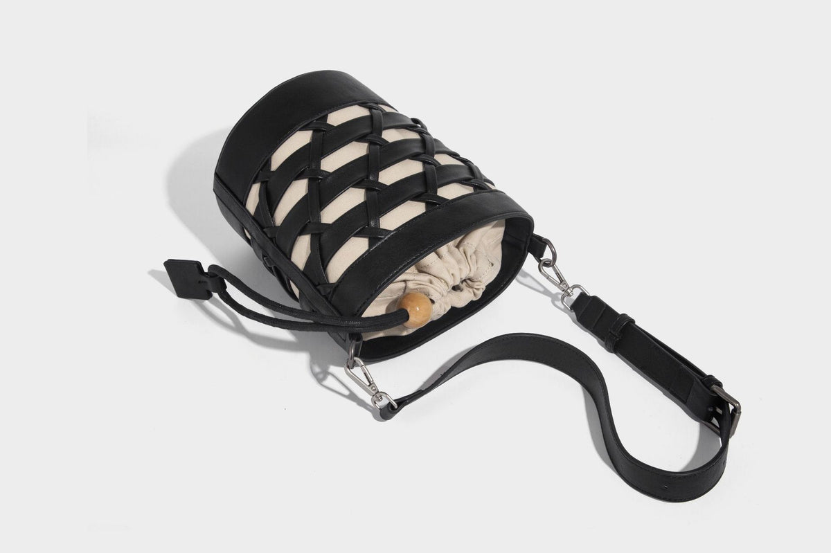 Small cylindrical woven lattice bucket bag with leather-look black trim, beige canvas body, wooden bead drawstring closure