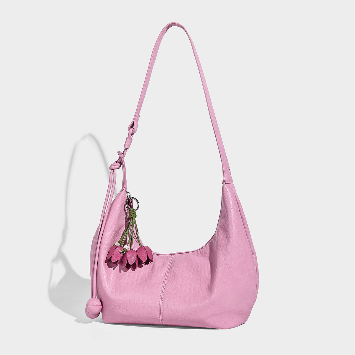 Slouchy crescent half-moon shoulder bag in pink pebbled textured finish with floral charm and knotted side detail, front view