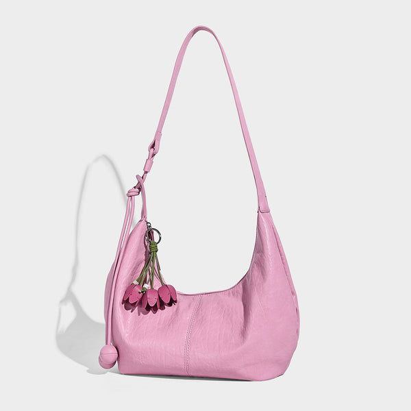 Slouchy crescent half-moon shoulder bag in pink pebbled textured finish with floral charm and knotted side detail, front view