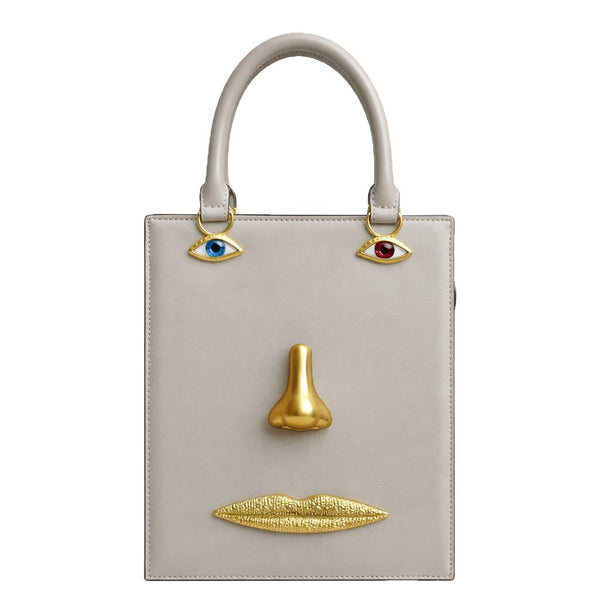 Structured rectangular top-handle bag in tan leather-look finish with gold-tone sculptural face hardware including