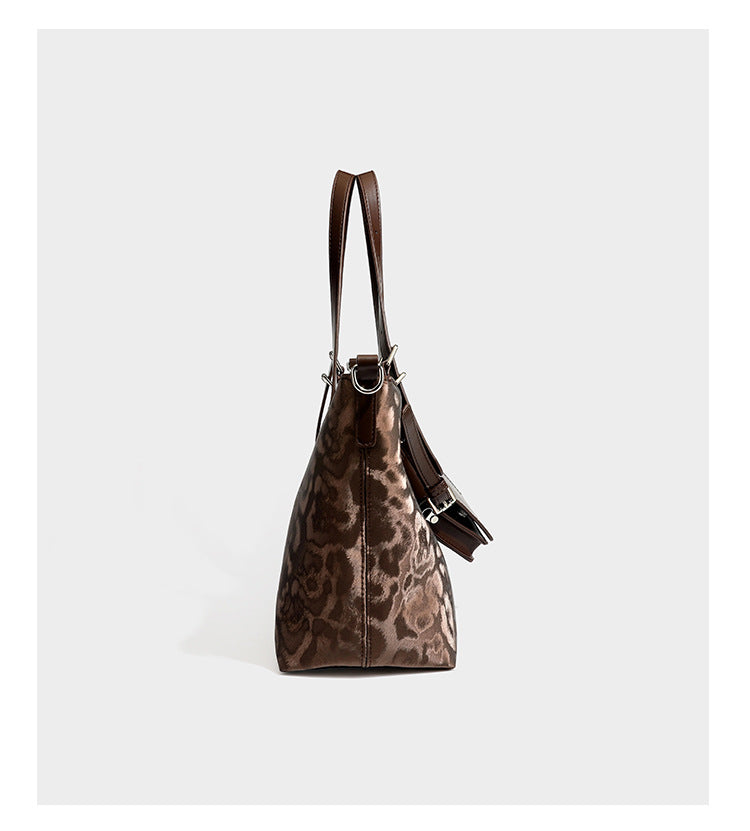 Glossy leopard-print tote bag with leather-look dark trim, dual top handles, detachable shoulder strap, and attached front