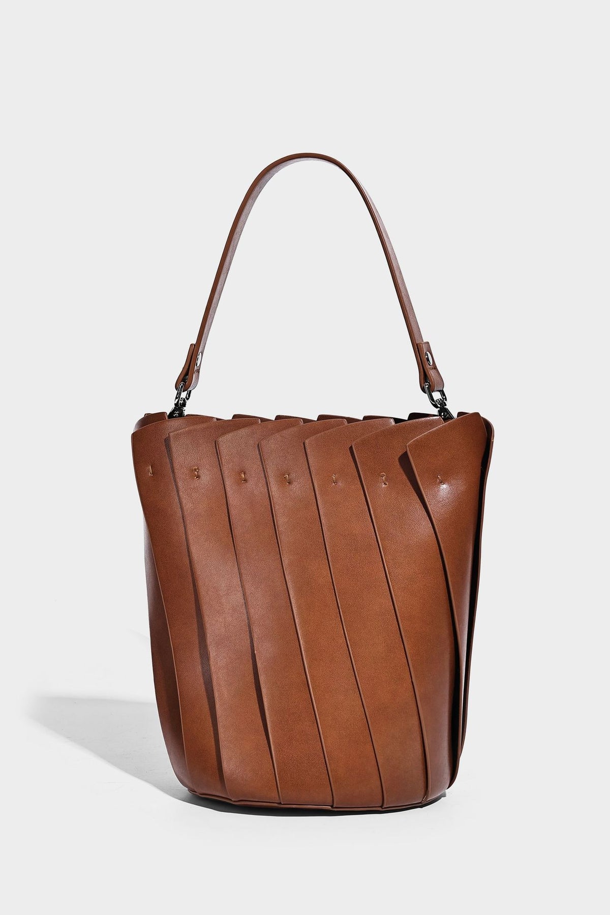 Structured pleated-panel bucket bag with curved top handle and detachable adjustable shoulder strap in smooth matte, detail