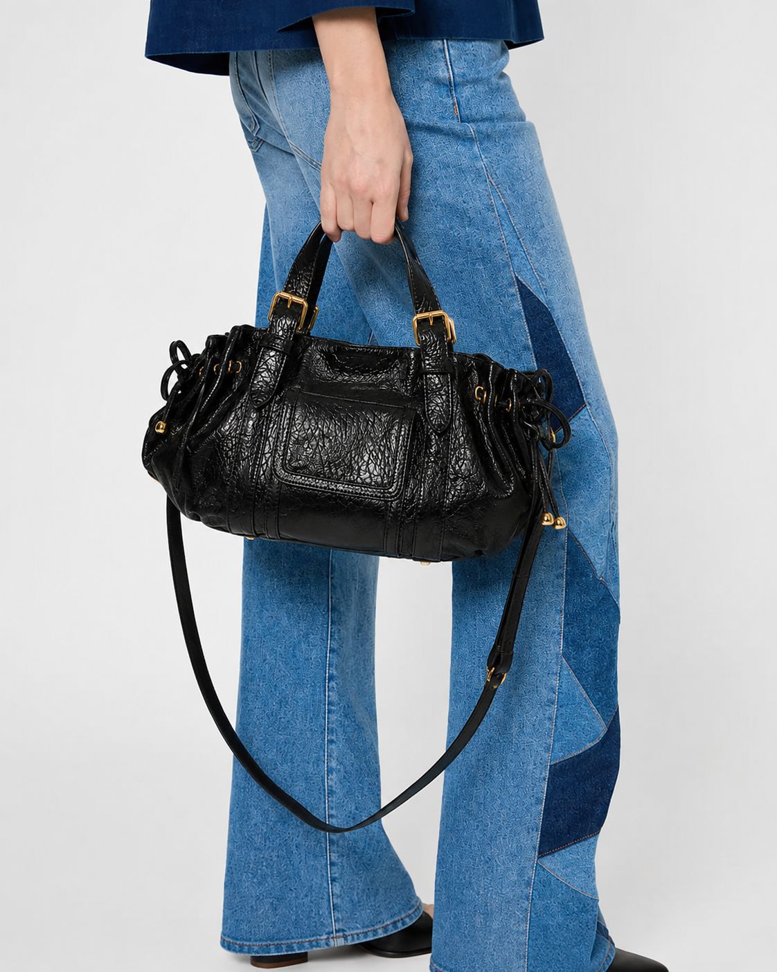 Schwarze Henkeltasche in geknitterter Glanzlederoptik mit seitlichen Kordelzügen, Vordertasche mit Schnalle, zwei Tragegriffen und goldfarbenem