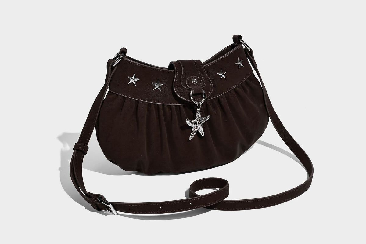 Ruched shoulder bag with curved flap, silver star studs, dangling starfish charm, and adjustable crossbody strap, detail view