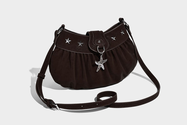 Ruched shoulder bag with curved flap, silver star studs, dangling starfish charm, and adjustable crossbody strap, detail view