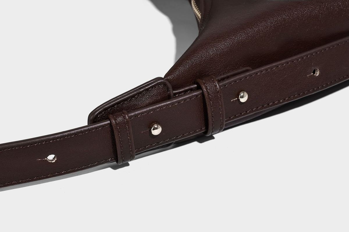 Lässig fallende, sichelförmige Hobo-Schultertasche in glatter dunkelbrauner Lederoptik mit Logo-Anhänger in Goldoptik und verstellbarem Schulterriemen