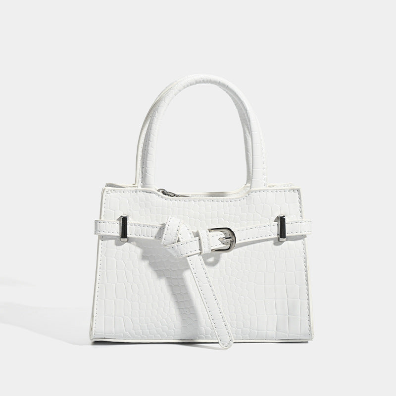 Small structured trapezoid mini top-handle bag with front belt-knot buckle detail and glossy leather-look finish, detail view