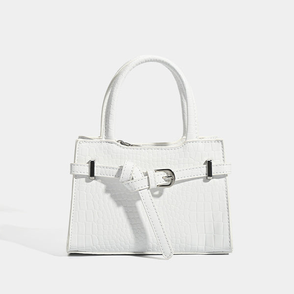 Small structured trapezoid mini top-handle bag with front belt-knot buckle detail and glossy leather-look finish, detail view