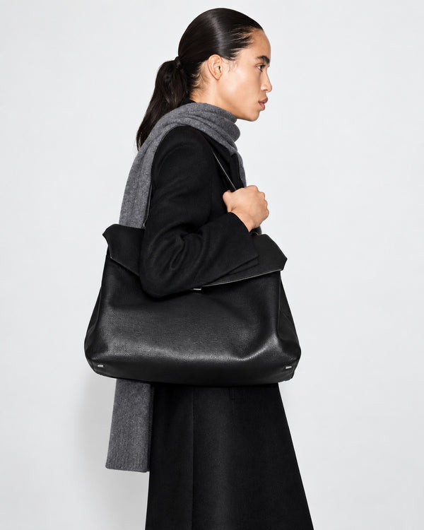 Large black slouchy leather-look shoulder bag with V-shaped envelope flap, silver-tone clasp, and adjustable strap, detail