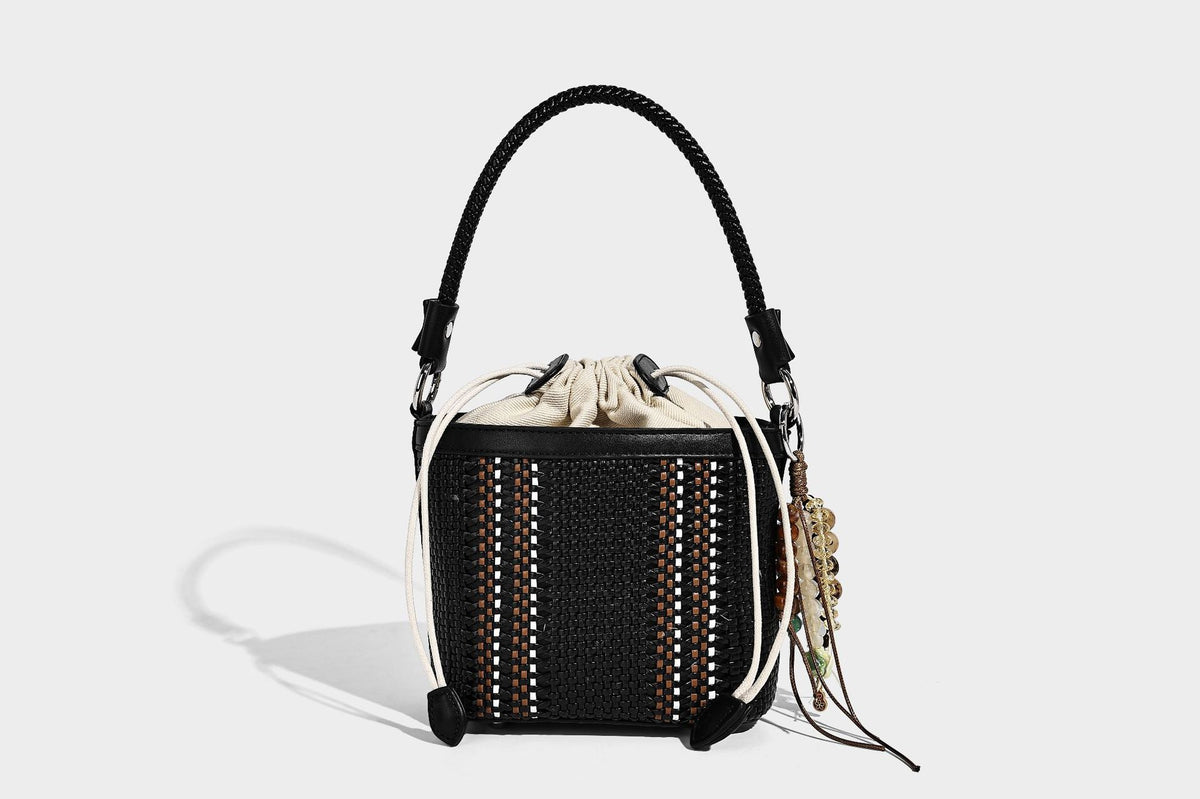 Small woven bucket bag with drawstring top, braided handle, detachable crossbody strap, and silver-tone ring hardware, detail