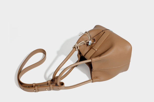 Pebbled leather-look bucket tote bag with rolled double handles, drawstring closure, braided cord charm, and detachable