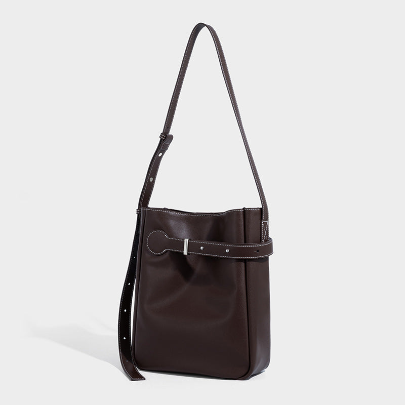 Structured dark brown leather-look bucket bag with white contrast stitching, front wraparound belt buckle strap, and long