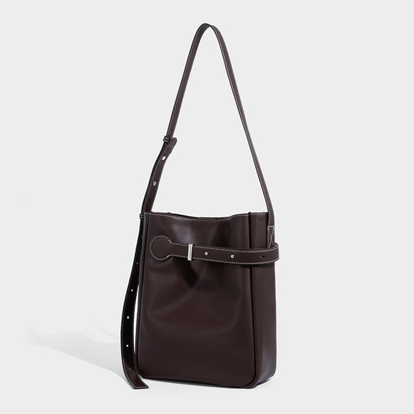 Structured dark brown leather-look bucket bag with white contrast stitching, front wraparound belt buckle strap, and long
