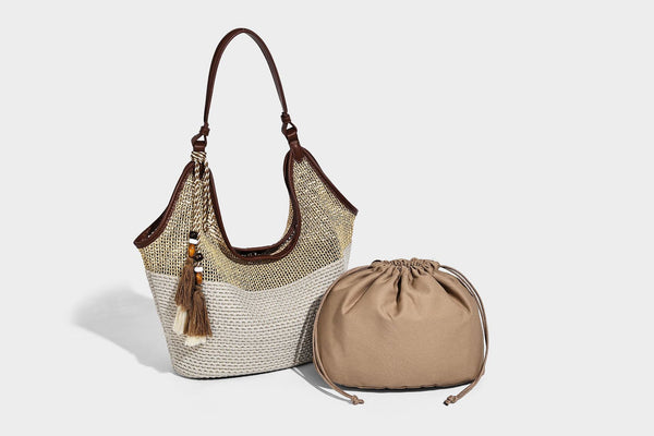 Two-tone beige and cream woven straw hobo shoulder bag with brown leather-look trim, long shoulder strap, and tassel-bead