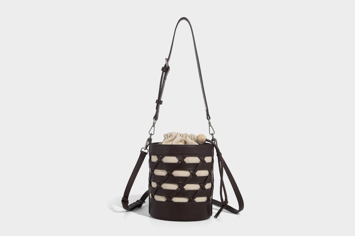 Small cylindrical woven lattice bucket bag with leather-look black trim, beige canvas body, wooden bead drawstring closure
