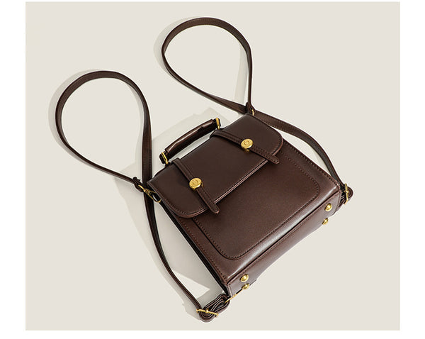 Structured mini satchel backpack with smooth leather-look finish, front flap pocket, gold-tone stud closures, and top handle