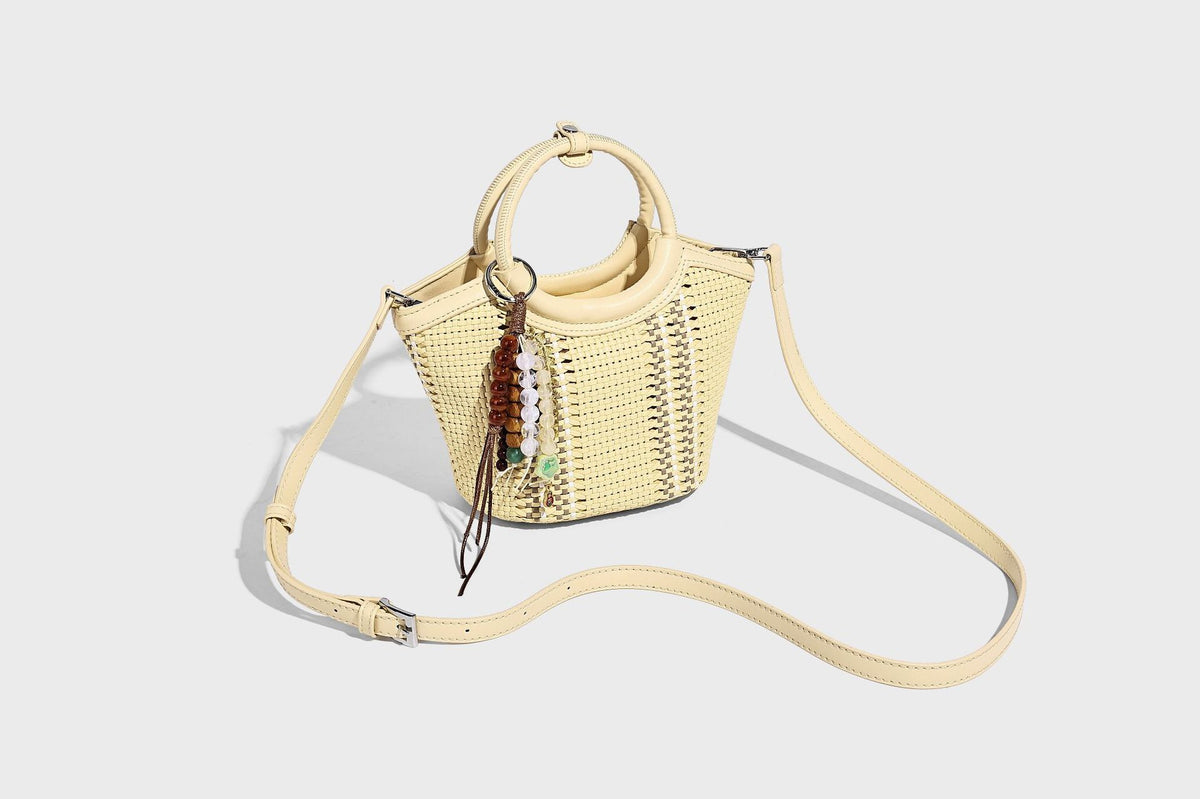Kleine strukturierte Beuteltasche aus geflochtenem Material mit rundem Tragegriff in Lederoptik, silberfarbenen Beschlägen und perlenbesetztem Quastenanhänger, Detail