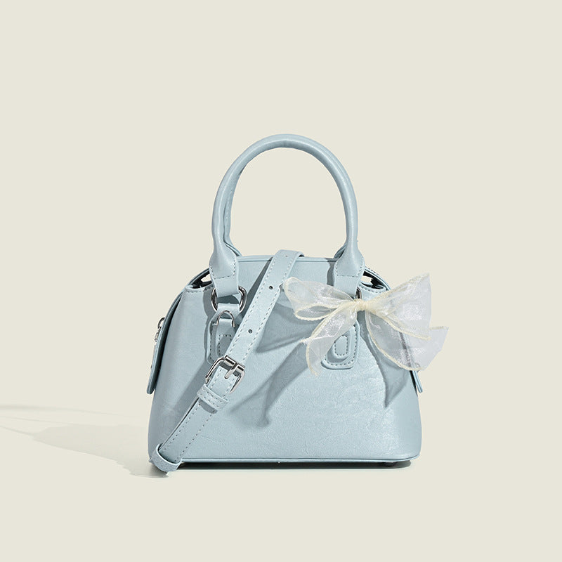 Small structured Boston bag in cream with glossy crinkled finish, sheer bow accent, silver-tone hardware, dual top handles