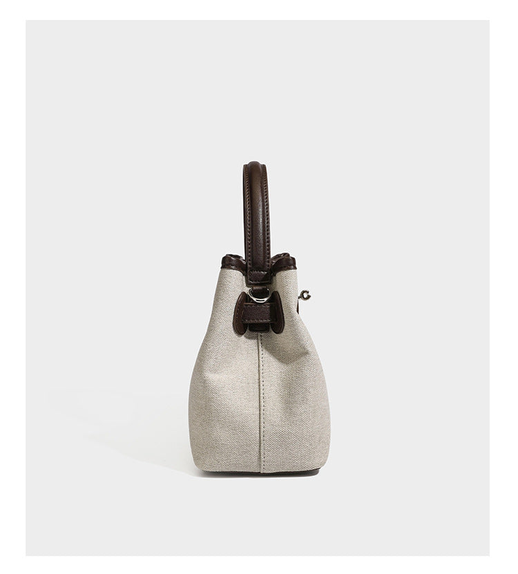 Small structured beige canvas top-handle bag with dark brown leather-look trim, silver turn-lock hardware, and detachable
