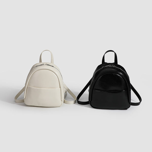Kompakter, abgerundeter Mini-Rucksack im Lederlook mit glänzender Oberfläche, Reißverschluss oben, Vordertasche und Tragegriff oben, Detailansicht