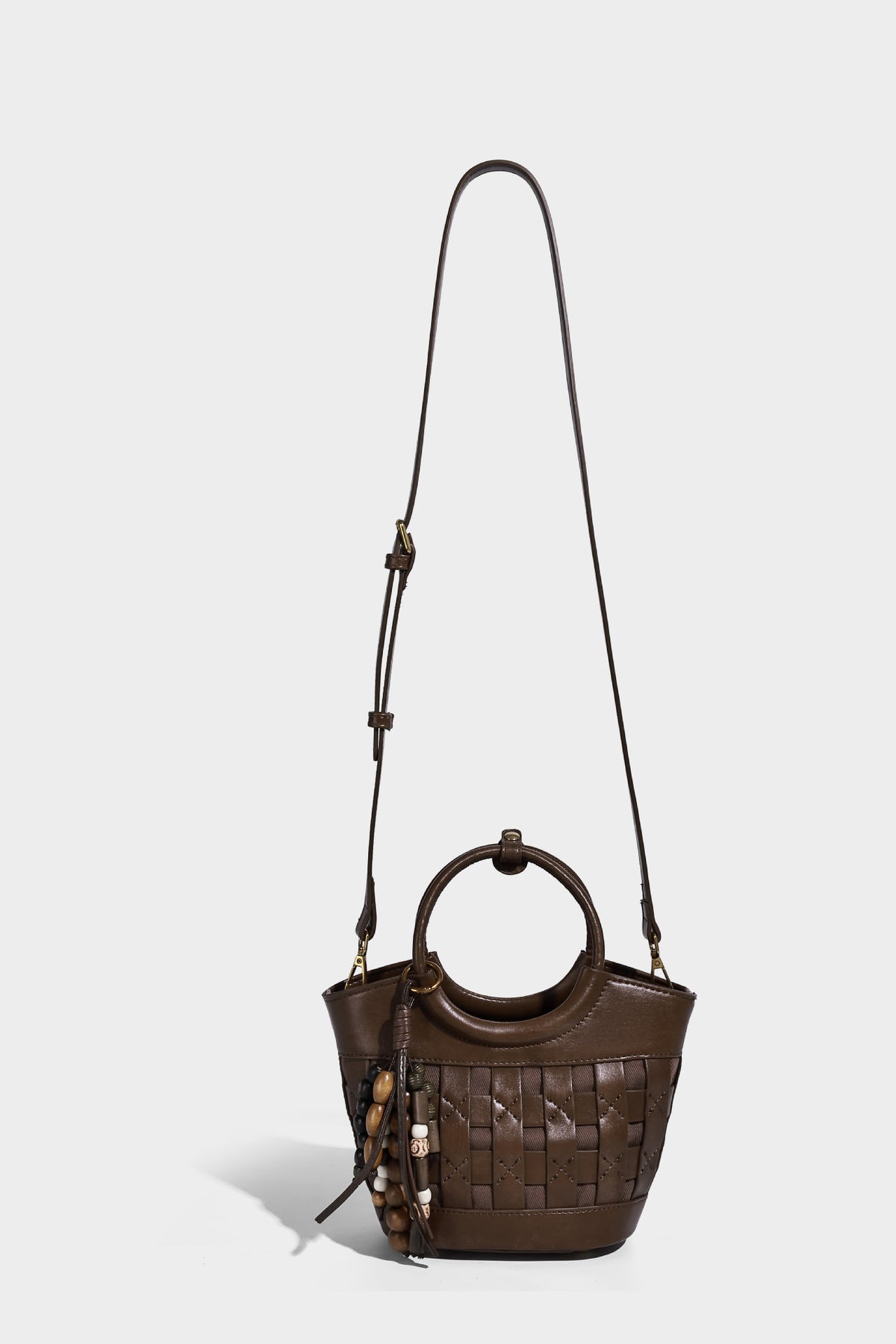 Small woven-panel bucket bag with circular ring handles, beaded tassel charm, and detachable crossbody strap in brown, detail