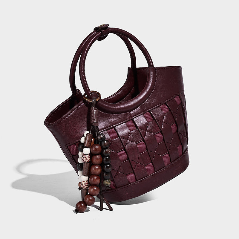 Small woven-panel bucket bag with circular ring handles, beaded tassel charm, and detachable crossbody strap in brown, detail