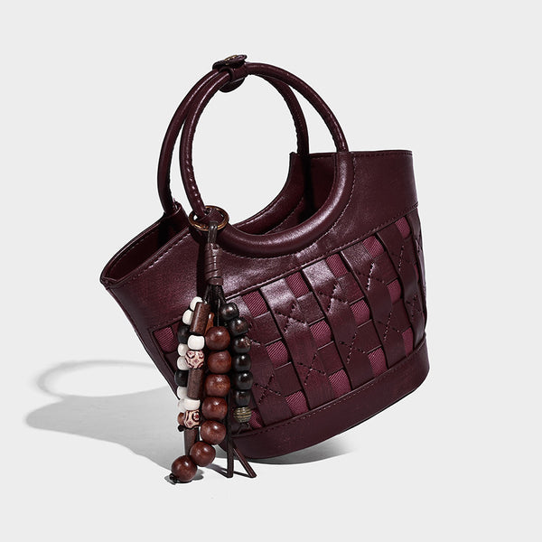 Small woven-panel bucket bag with circular ring handles, beaded tassel charm, and detachable crossbody strap in brown, detail