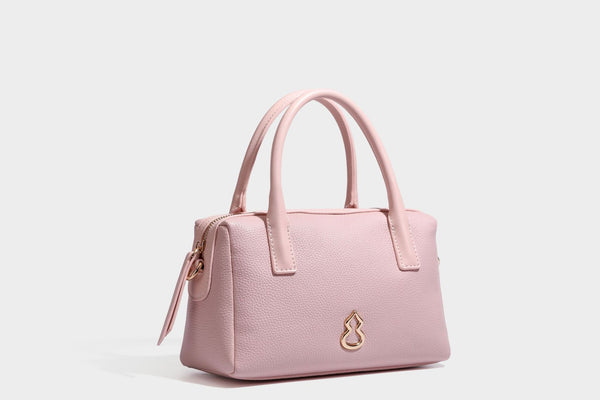 Small structured pillow satchel bag with pebbled leather-look finish, dual rolled top handles, gold-tone gourd emblem, and