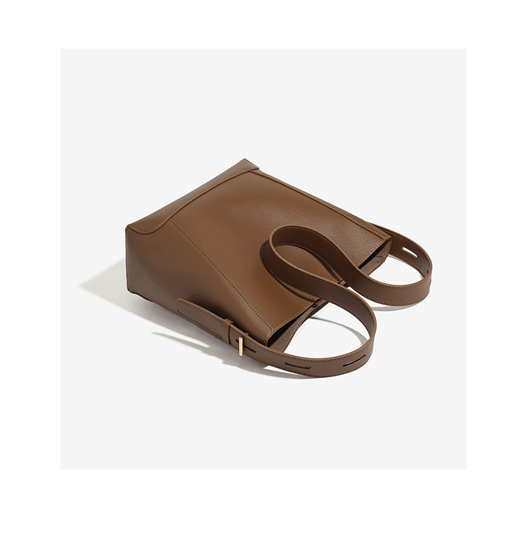 Structured smooth leather-look bucket shoulder bag with long adjustable strap and gold-tone buckle hardware in brown, detail