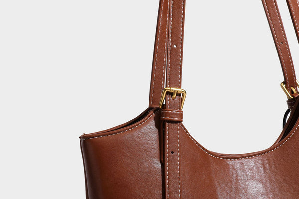 Structured smooth leather-look tote bag with long shoulder strap, gold-tone hardware, and hanging tassel-coin charm, detail