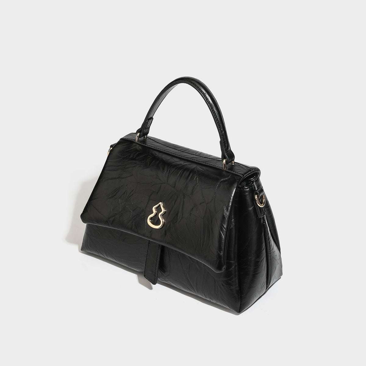 Structured black satchel bag with glossy crinkled leather-look finish, gold-tone emblem flap closure, slim top handle, and
