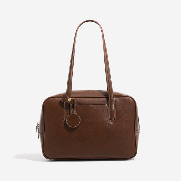 Structured boxy bowling-style tote bag in deep brown leather-look finish with dual top handles, front slip pocket, round