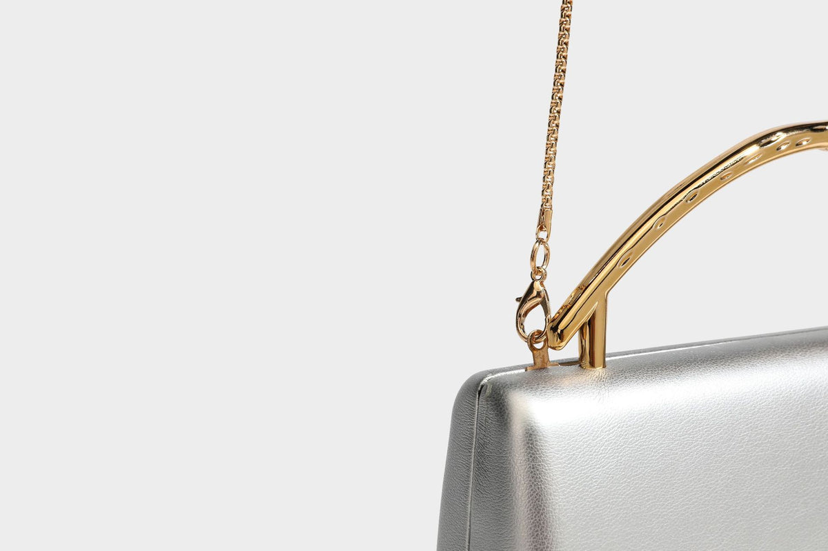 Strukturierte rechteckige Clutch mit goldfarbenem Henkel in Form einer Rosenknospe und abnehmbarem Kettenriemen in Metallic-Optik, Detailansicht