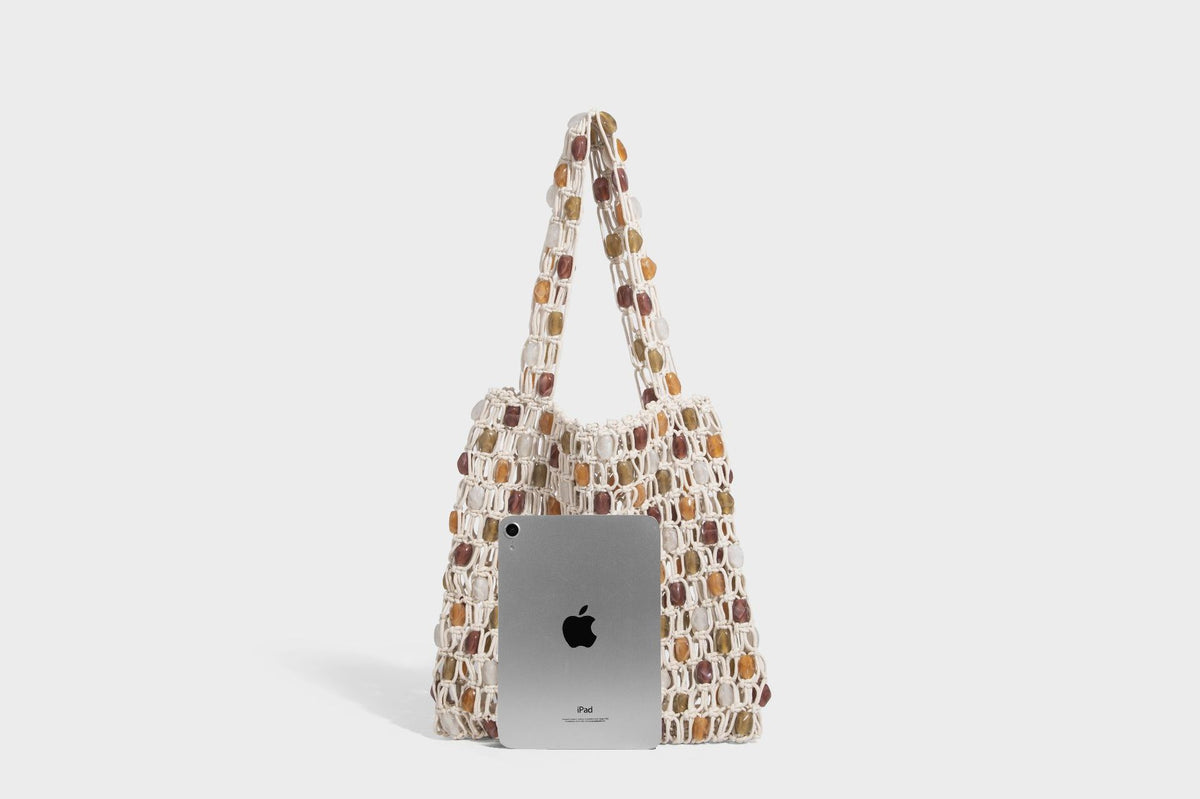 Cream macramé open-weave tote bag with multicolor amber olive and translucent bead accents and woven shoulder straps, detail