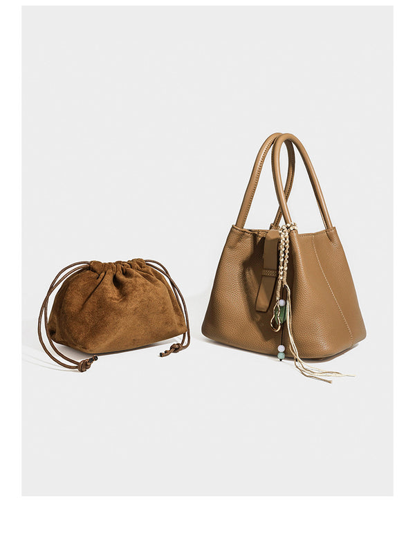 Pebbled leather-look bucket tote bag with rolled double handles, drawstring closure, braided cord charm, and detachable
