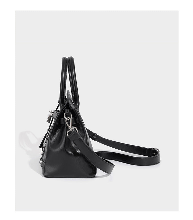 Structured black leather-look satchel bag with silver padlock hardware, front zip pockets, key charms, and top handles