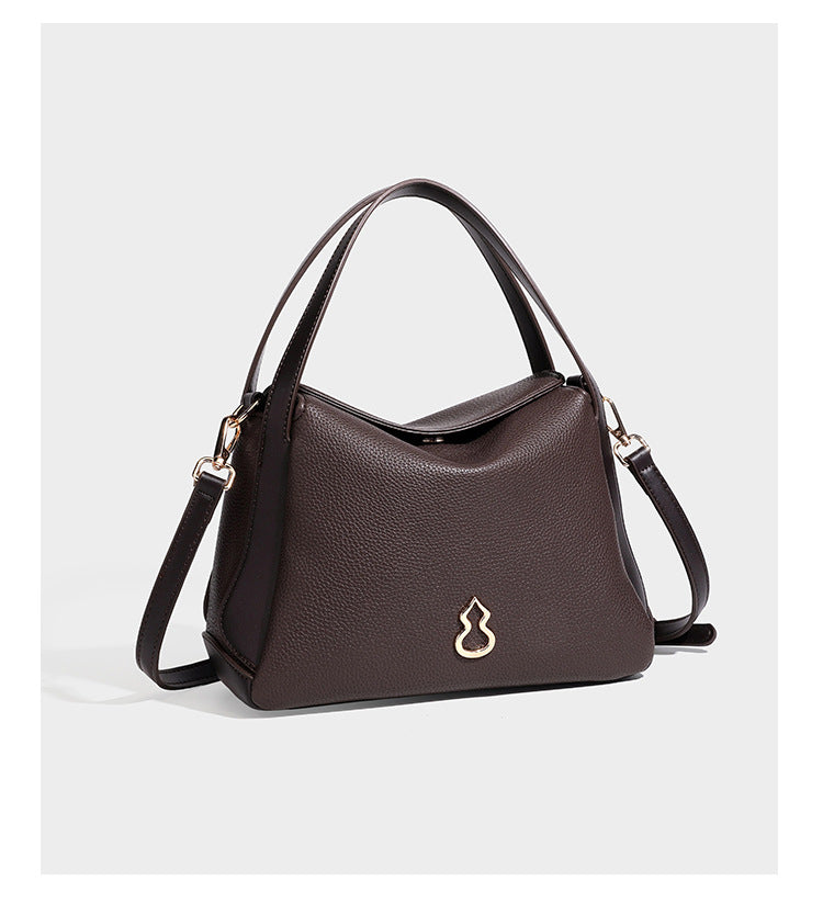 Structured pebbled leather-look shoulder bag with flap top, gold-tone emblem hardware, dual top handles, and detachable