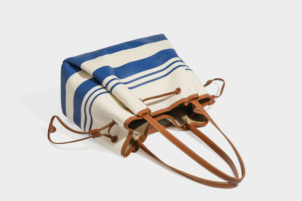 Large cream and navy striped canvas bucket tote bag with tan leather-look trim, drawstring closure, and double shoulder