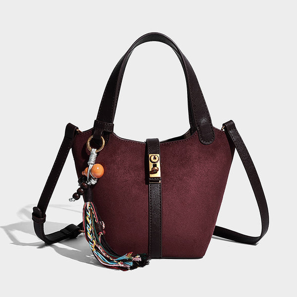 Small structured trapezoid tote bag in matte suede-look finish with black contrast trim, gold-tone front clasp, tassel charm