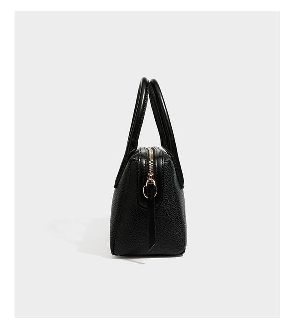 Small structured pillow satchel bag with pebbled leather-look finish, dual rolled top handles, gold-tone gourd emblem, and