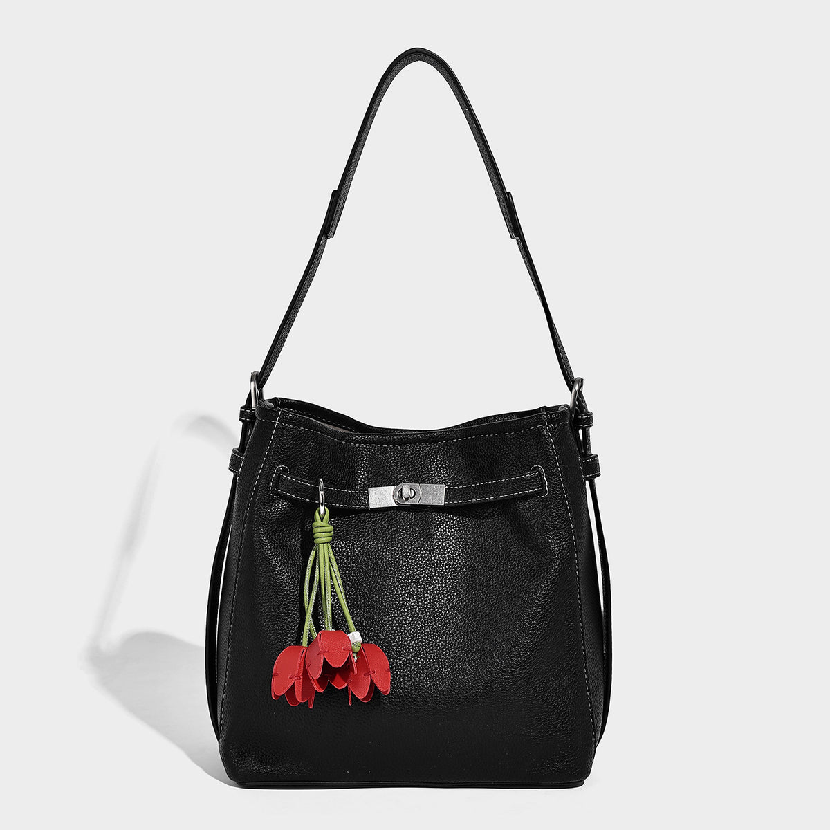 Soft-structured pebbled bucket shoulder bag with front turn-lock strap detail, adjustable strap, and hanging floral tassel